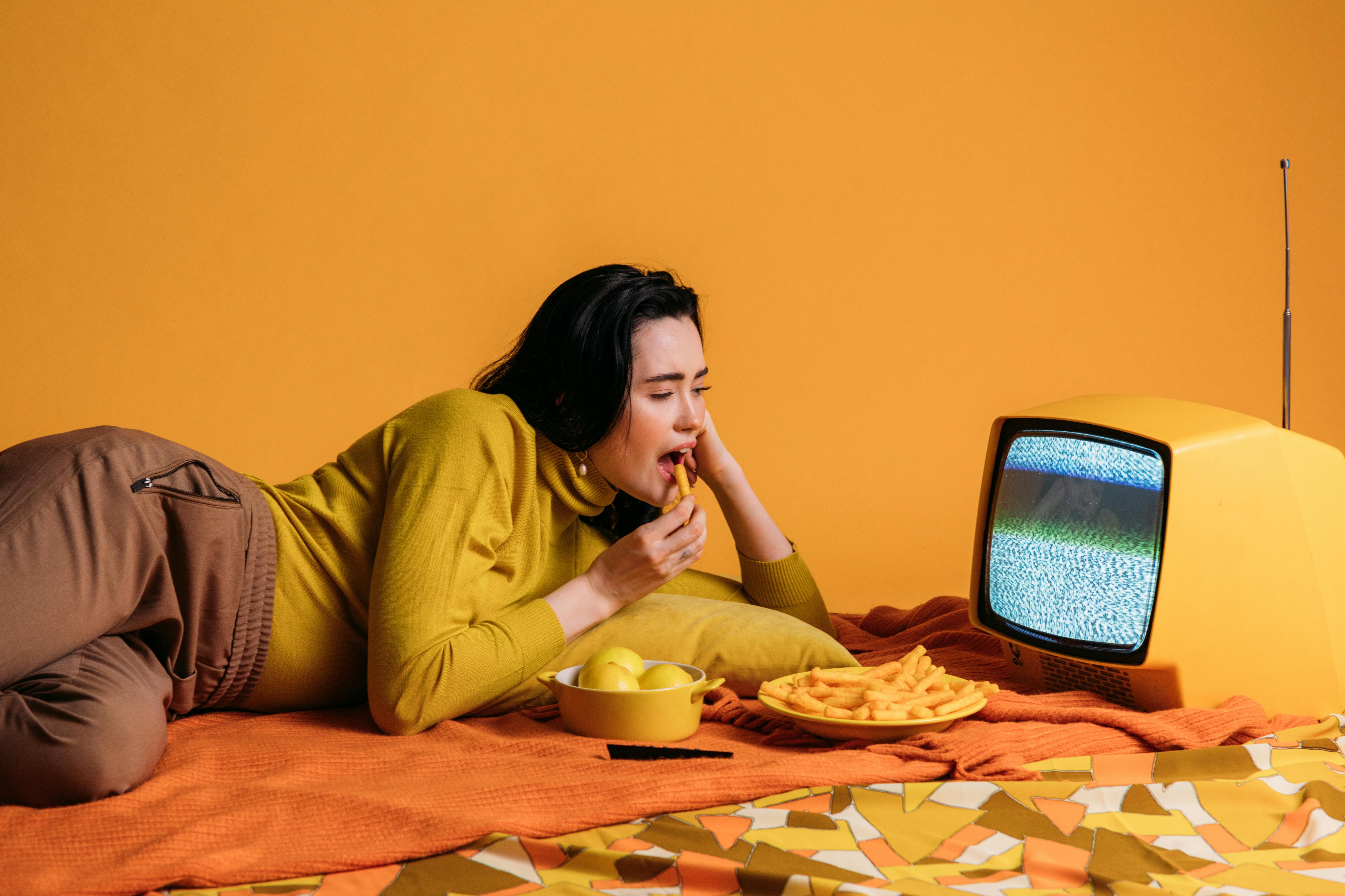 A woman emotionally eating in front of the TV, highlighting the challenges of managing food cravings while watching television.