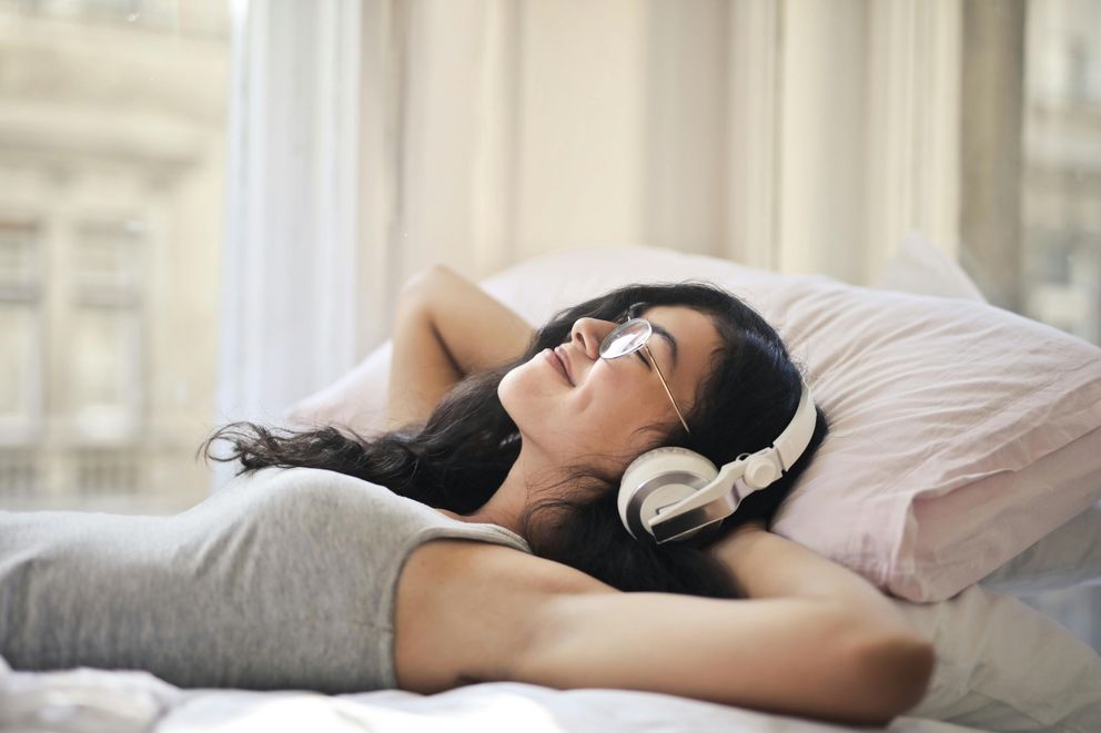 A woman relaxing before bed, listening to soothing sounds to enhance sleep quality and reduce stress.