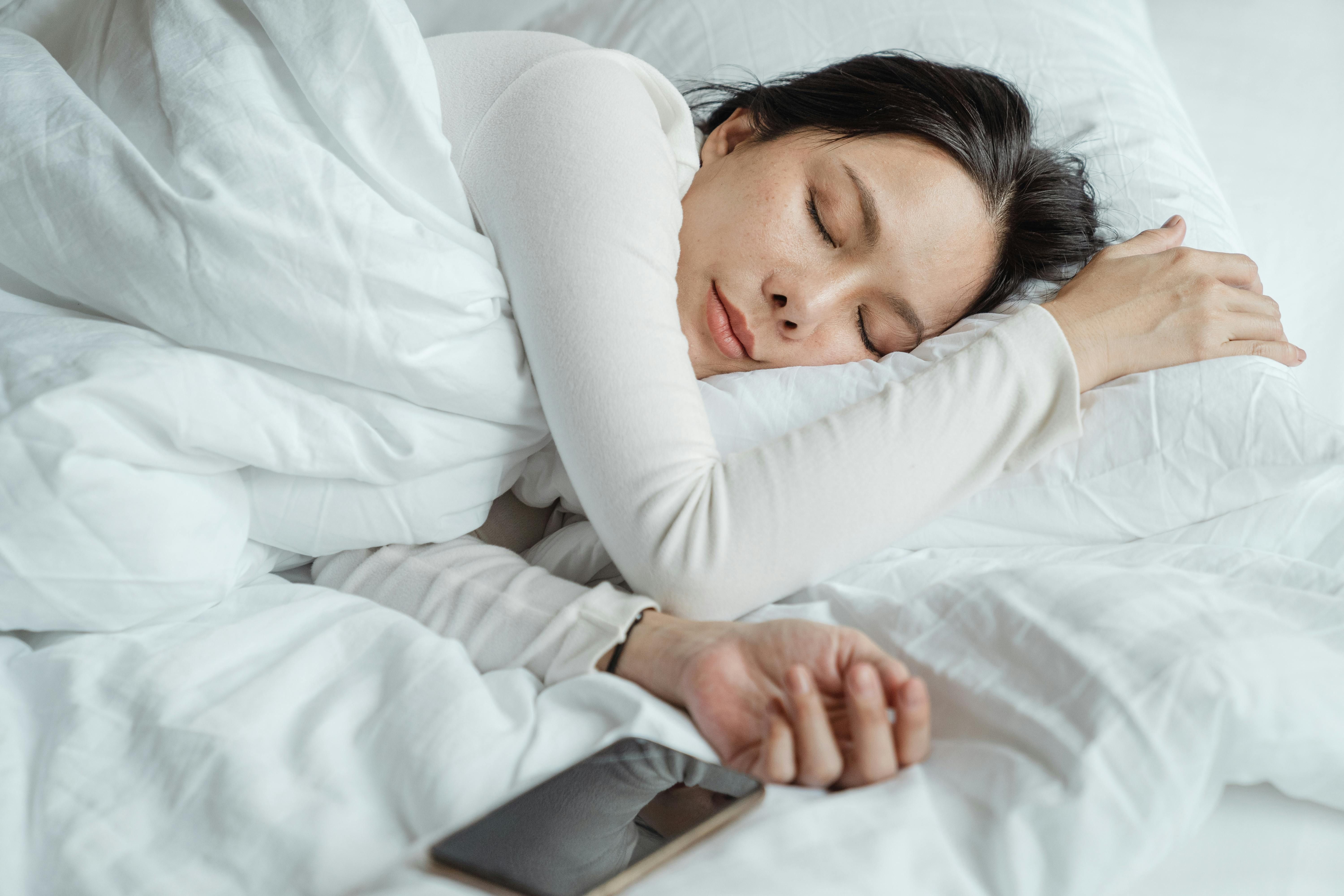 A woman happily sleeping in a hotel bed, prioritizing rest and sleep for a healthy weight loss journey while traveling.