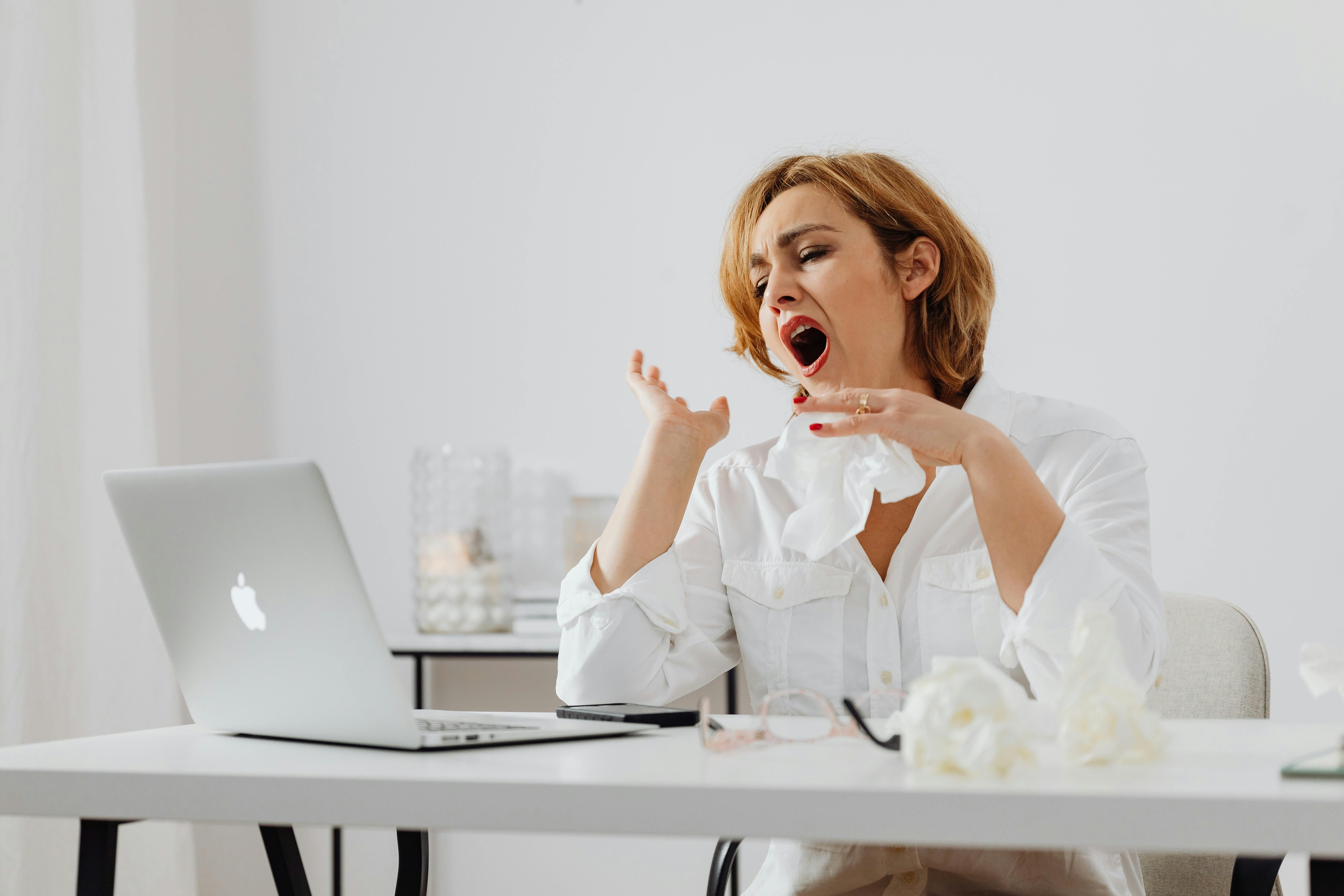 A woman yawning at her desk while working on her computer, experiencing an afternoon energy slump.