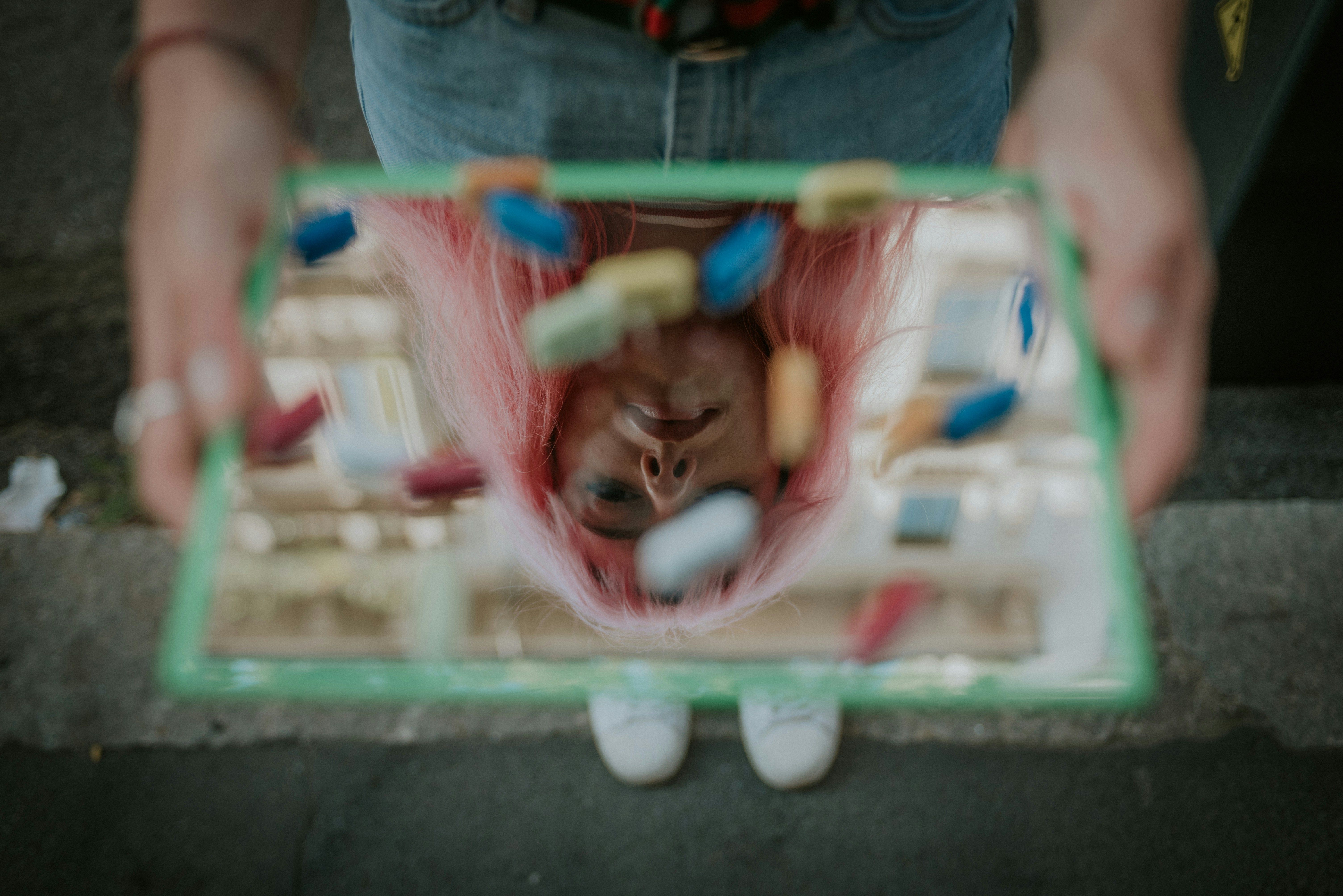 Woman holding pills reflected in a mirror.